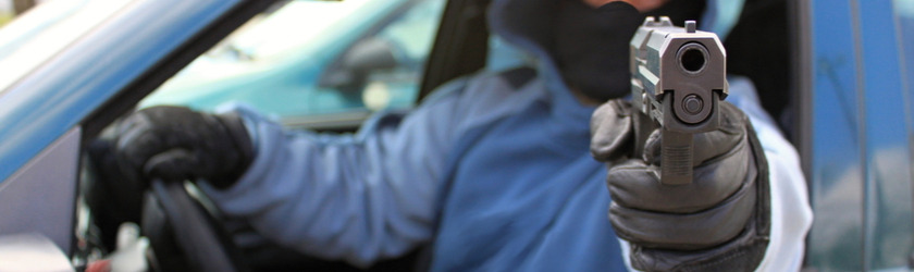 Person driving a car with one hand and aiming a gun out the window with the other hand