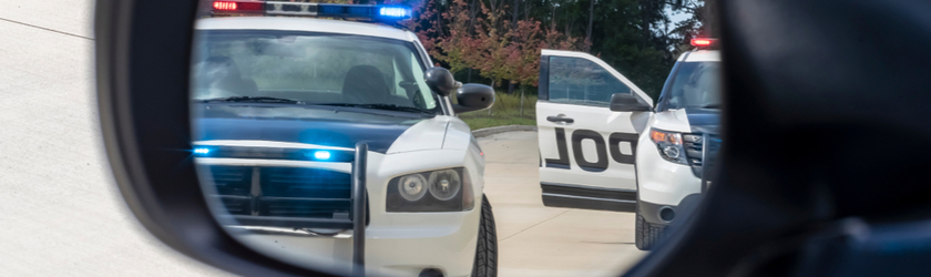 Two police cars are reflected in a car's driver side view mirror