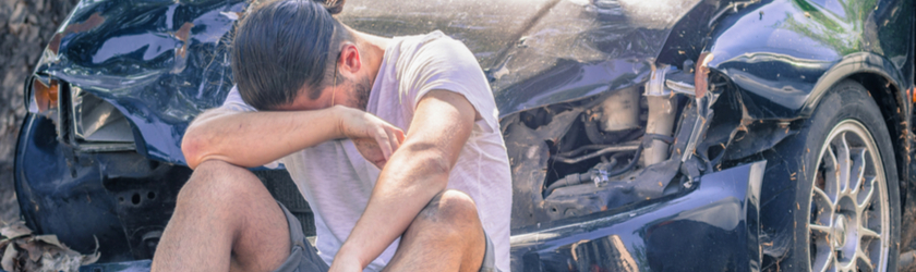 A man sits crying in front of his badly wrecked car